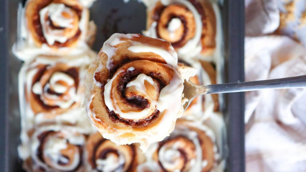 A spoon lifting up a piece of cinnamon roll.