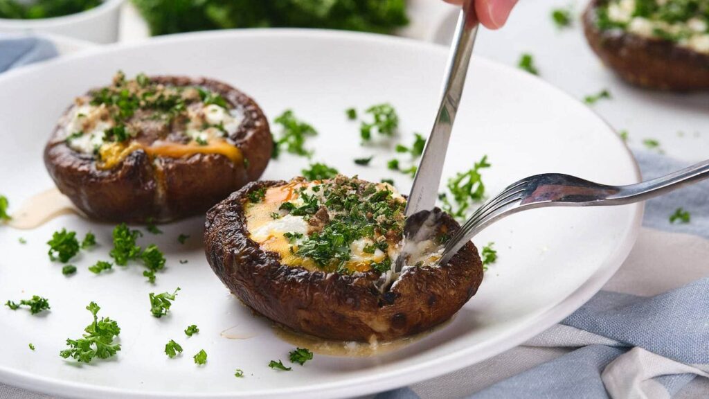 A hand grips a fork, hovering over a stuffed mushroom.