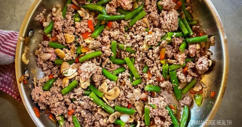 Cooked ground beef with string beans in a skillet.