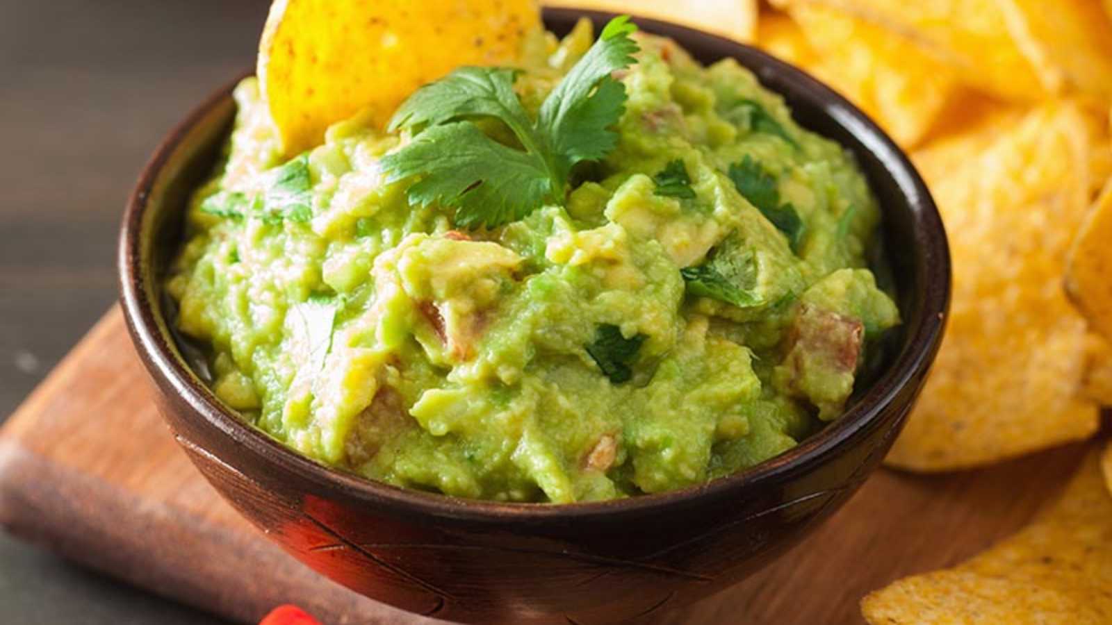 A bowl of guacamole garnished with cilantro and an upright tortilla chip.