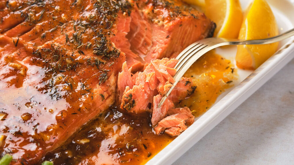 A fork holding a piece of salmon with sauce on a white plate.