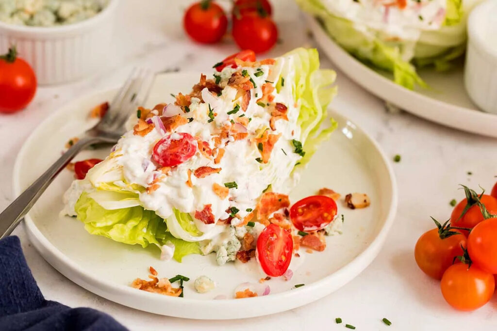 Iceberg wedge salad topped with blue cheese, bacon, cherry tomatoes, and chives.