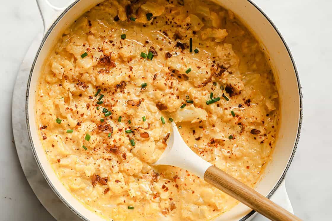 Cauliflower cheddar cheese bacon soup in a pot with a spoon.