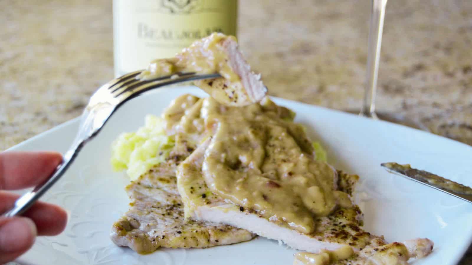 A plate of sliced pork with mushroom sauce, fork above, and wine bottle behind.