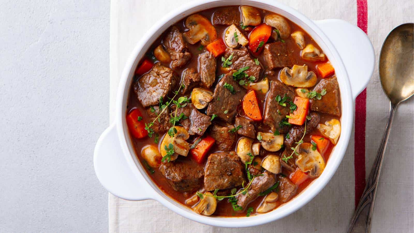 Beef stew in a white pot served with a spoon.