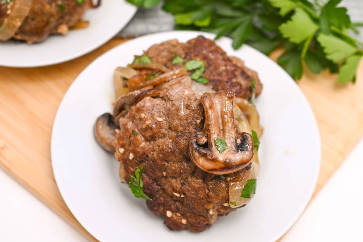 White plate with salisbury steak on it and a mushroom on top of them.