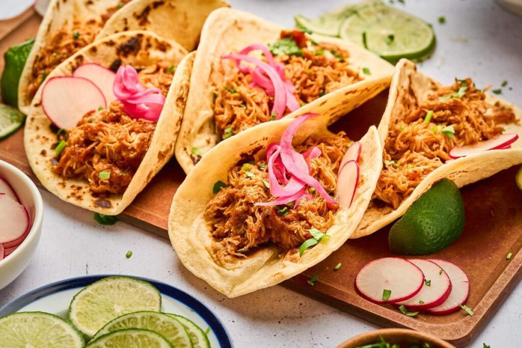 Four tacos with Instant Pot chicken tinga, topped with pickled onions and radishes.