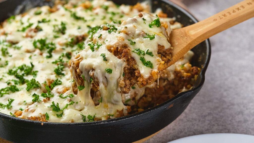 A wooden spoon lifting a poriton of italian ground beef skillet.
