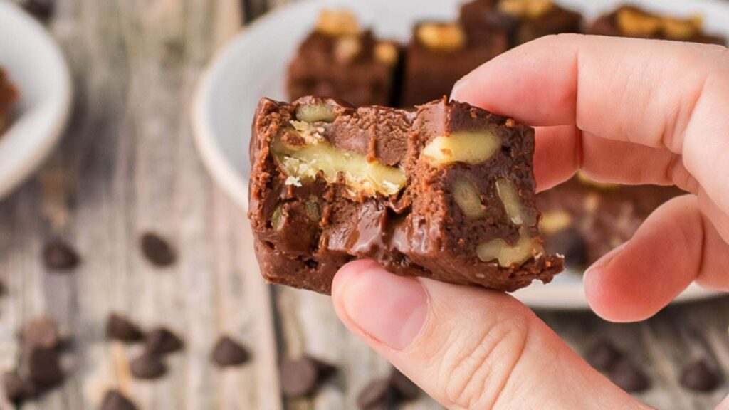 A person's hand holding up a piece of fudge with a bite taken out of it.