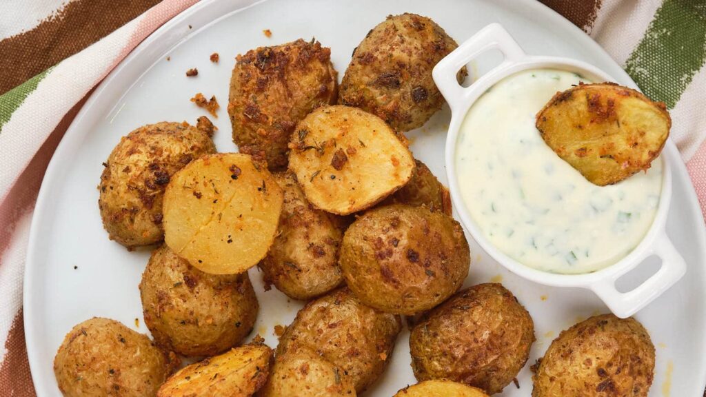Cripsy parmesan potatoes on a white plate, with a small bowl of sauce next to it.
