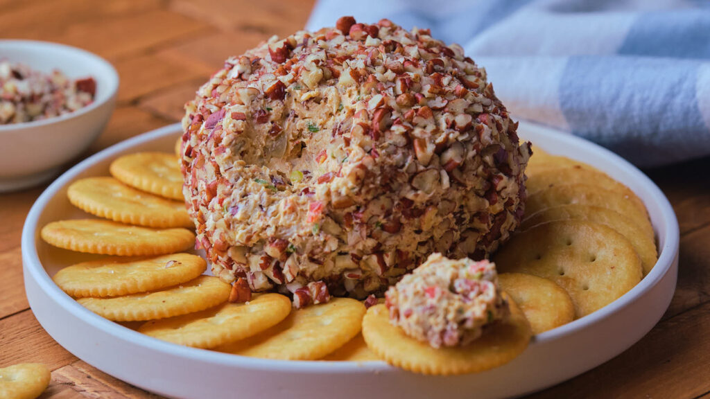 A pineapple cheeseball surrounded by crackers on a white plate.