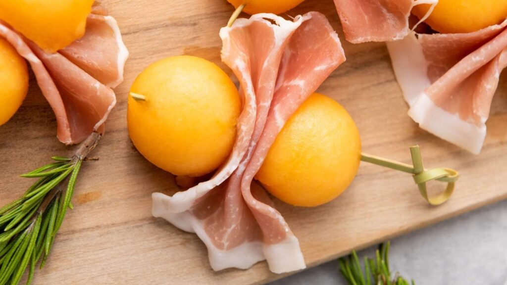 A piece of prosciutto e melone on a wooden board.