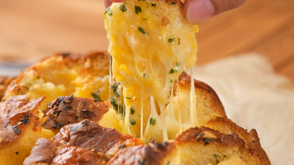 A person's hand pulling a piece of cheesy bread.