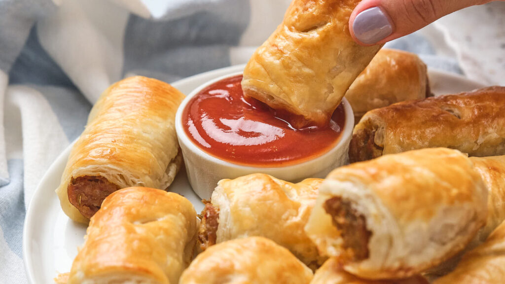 A sausage roll being dipped in red sauce.