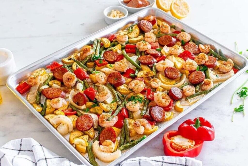 Sheet pan shrimp and sausage with bell peppers, onions, and squash, topped with fresh herbs.