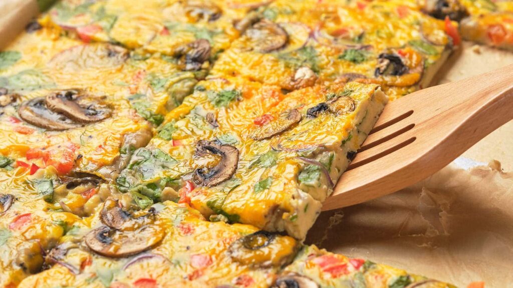 A slice of baked egg frittata topped with mushrooms and vegetables.