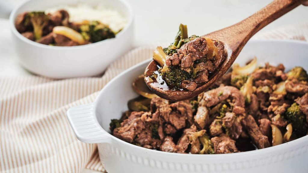 A wooden spoon lifting a portion of a beef and broccoli dish.
