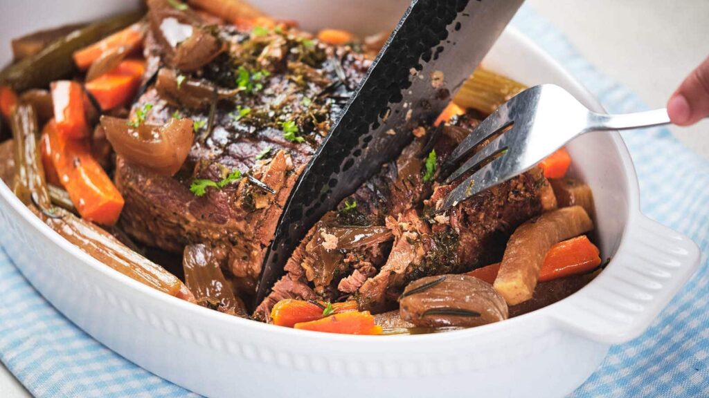 Pot roast being sliced in a baking dish.