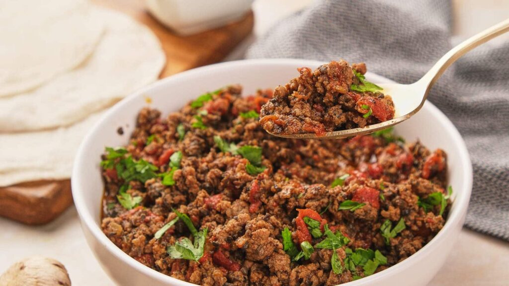 A bowl of taco meat, with a spoon lifiting a portion of it.