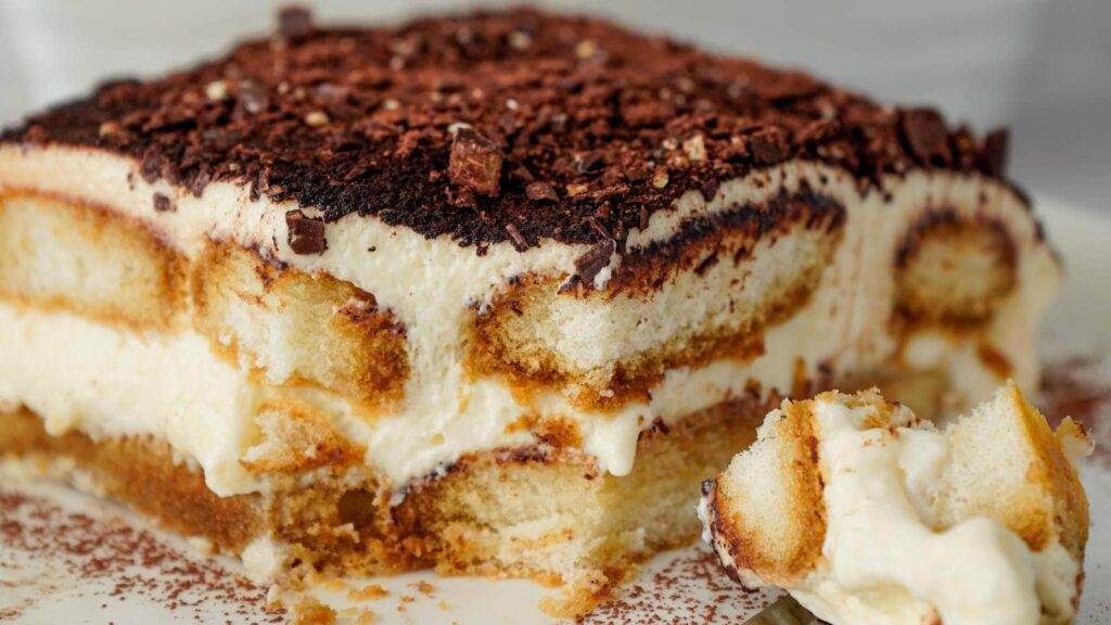 A piece of tiramisu with a bite taken out of it, showcasing a creamy layer and decorative icing on top.