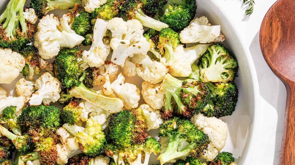 air fryer broccoli and cauliflower on a white plate with a pink linen and thyme.