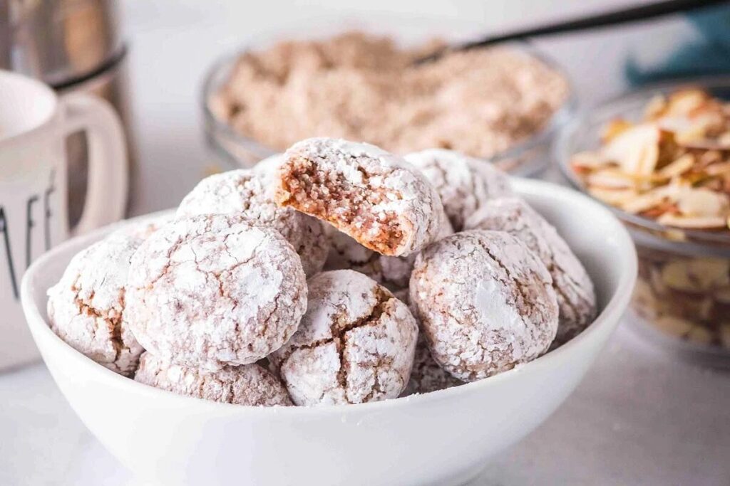 Gluten-free Amaretti Crinkle cookies dusted with powdered sugar, ideal for Christmas baking.