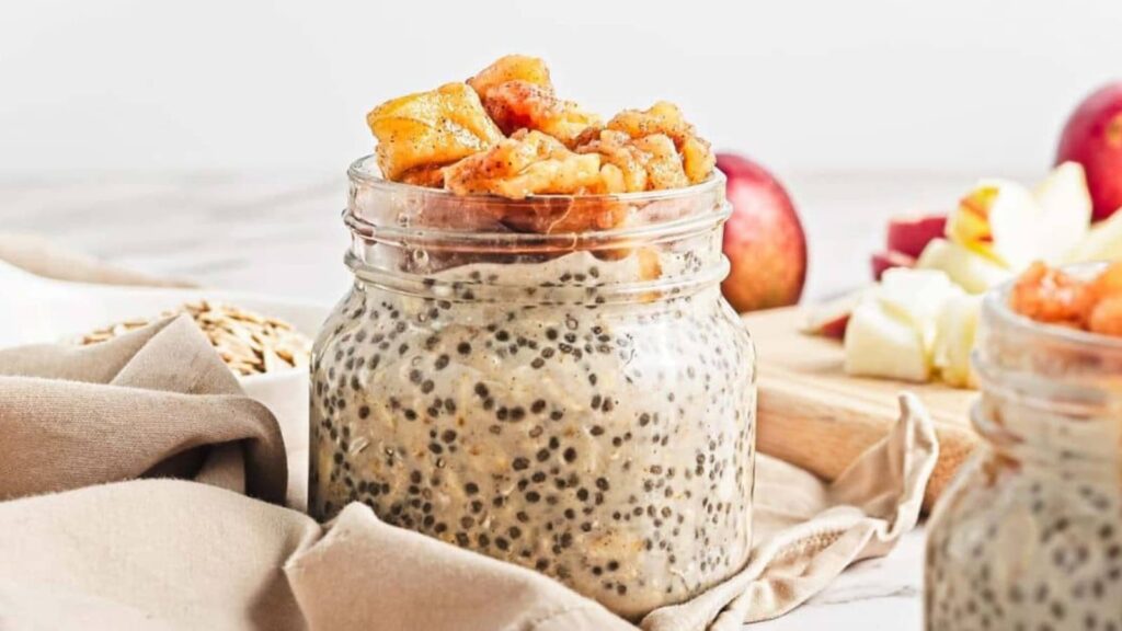 A jar of chia seed pudding topped with caramelized apple pieces, with apples in the background.