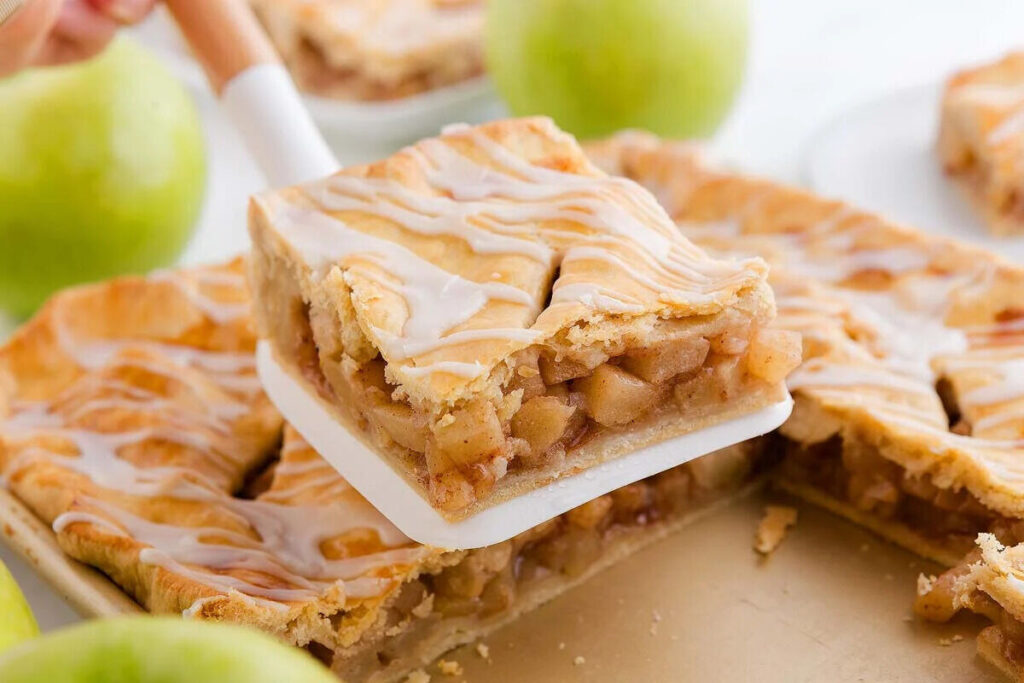 A slice of apple pie bars is being served with a spatula.