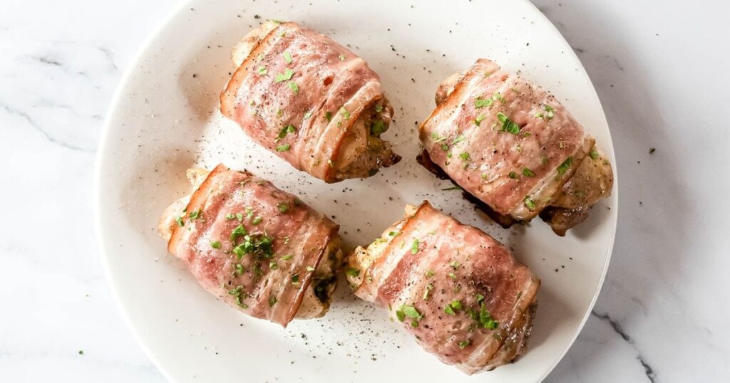 Three bacon-wrapped chicken rolls garnished with chopped herbs, served on a white plate.