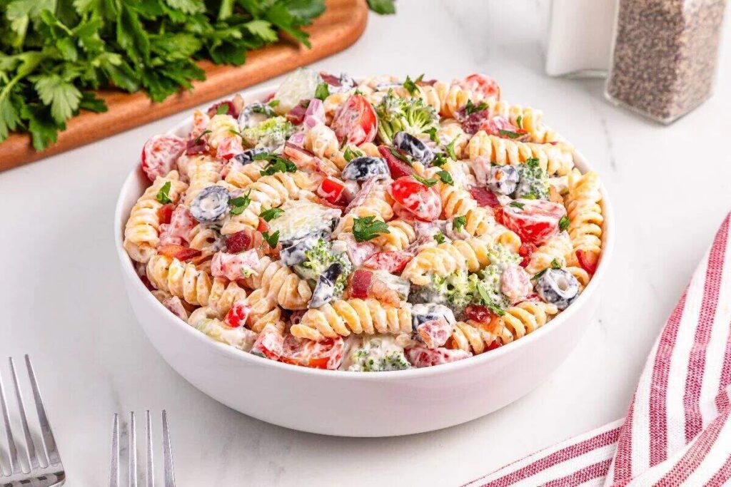 Creamy bacon ranch pasta salad with rotini, cherry tomatoes, broccoli, and fresh herbs.