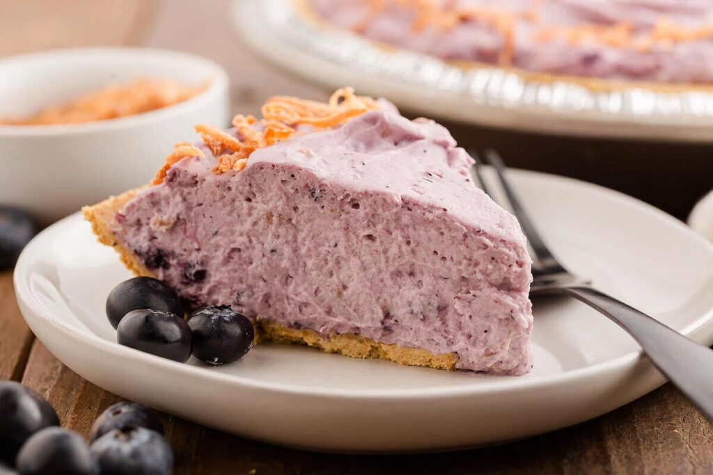 A slice of creamy blueberry pie on a white plate, garnished with fresh blueberries.