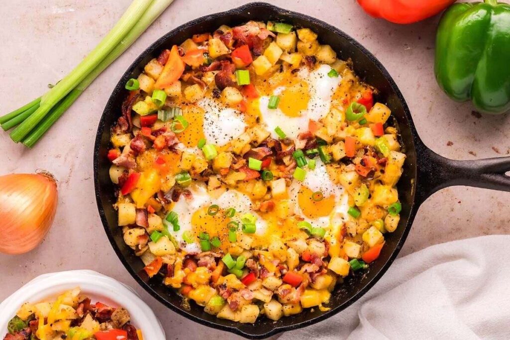 A hearty breakfast skillet filled with a cooked mixture of diced potatoes, bell peppers, bacon, cheese, and eggs.