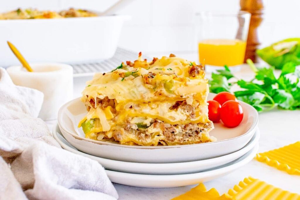 A slice of breakfast lasagna on a white plate with cherry tomatoes and greens.