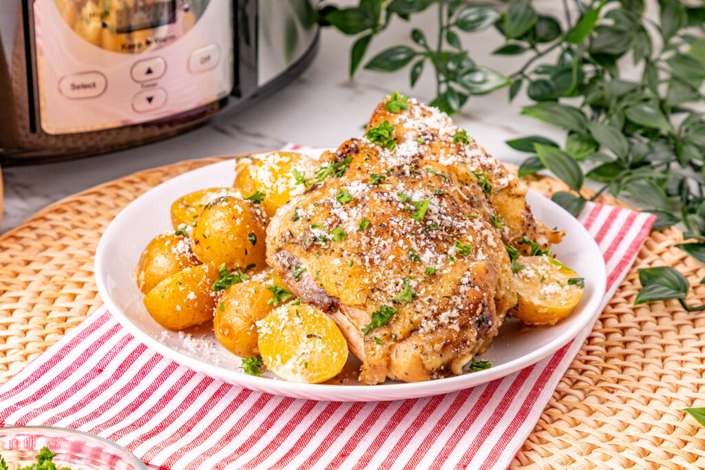 A plate of roasted chicken and baby potatoes, garnished with herbs and grated cheese, on a red-striped napkin.