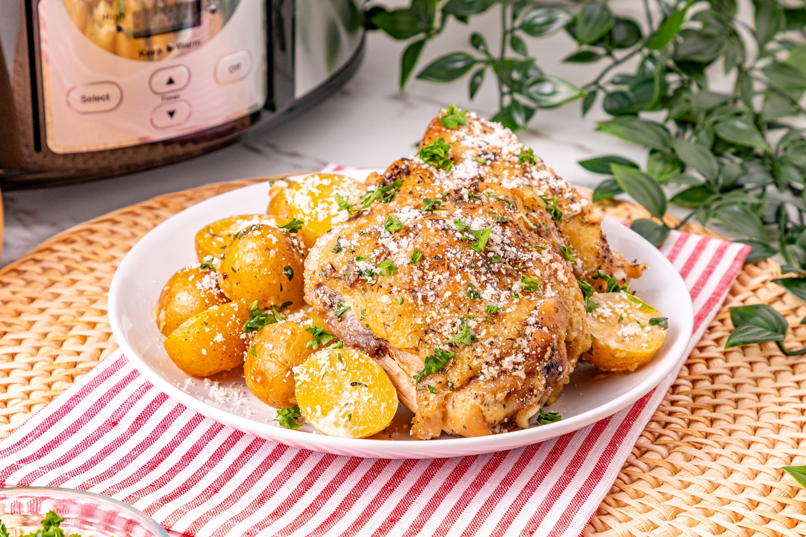 A plate of roasted chicken and baby potatoes, garnished with herbs and grated cheese, on a red-striped napkin.