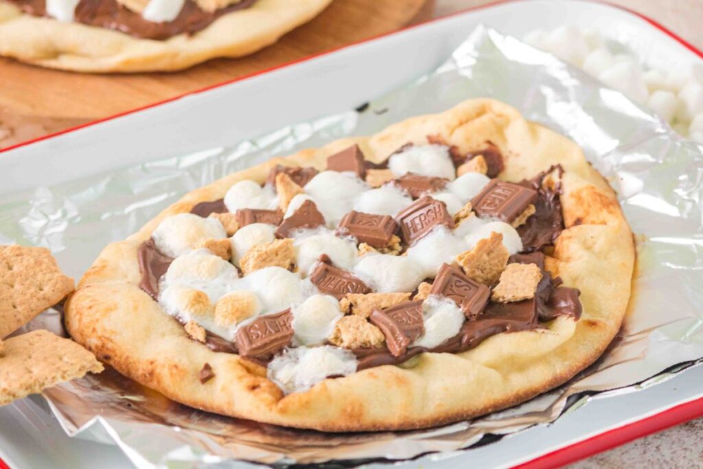 Naan bread topped with melted chocolate, marshmallows, and graham crackers just like a campfire s'mores pizza.