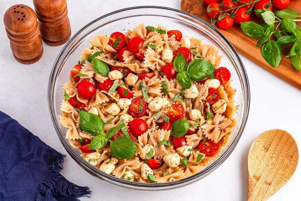 A colorful bowtie pasta salad with cherry tomatoes, mozzarella, and fresh basil in a glass bowl.