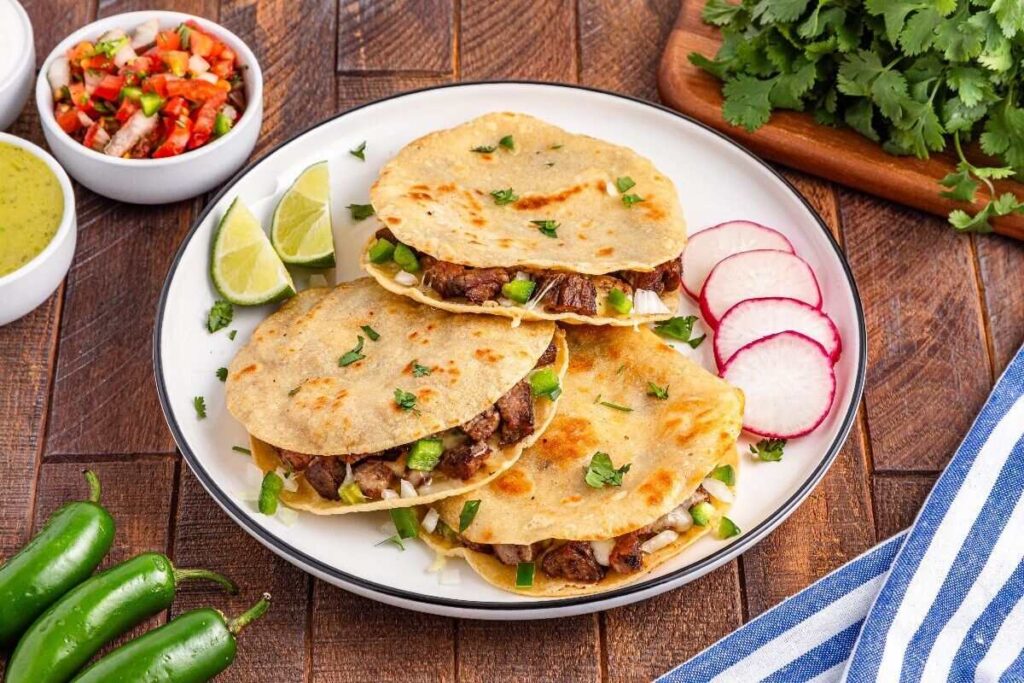 Three beef quesadillas served with lime, radish, salsa, and fresh cilantro.