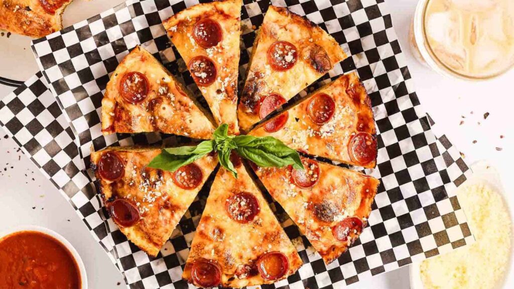Sliced pepperoni pizza on a checkered platter garnished with fresh basil.