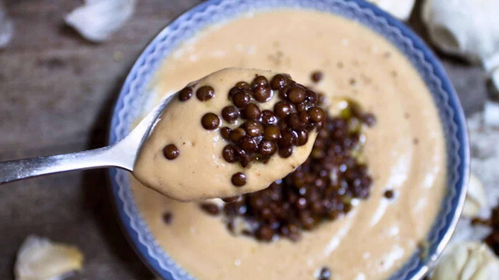A bowl of celery root soup topped with black lentils.
