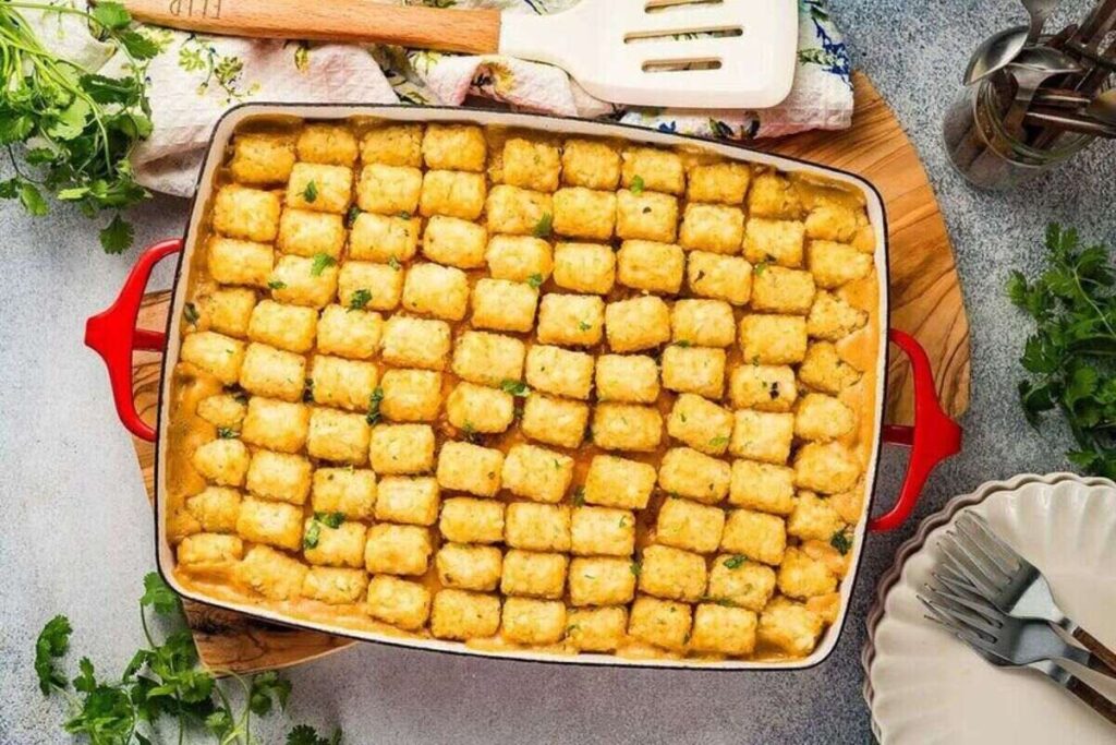 Tater tots layered over creamy chicken casserole on a wooden board, garnished with cilantro.