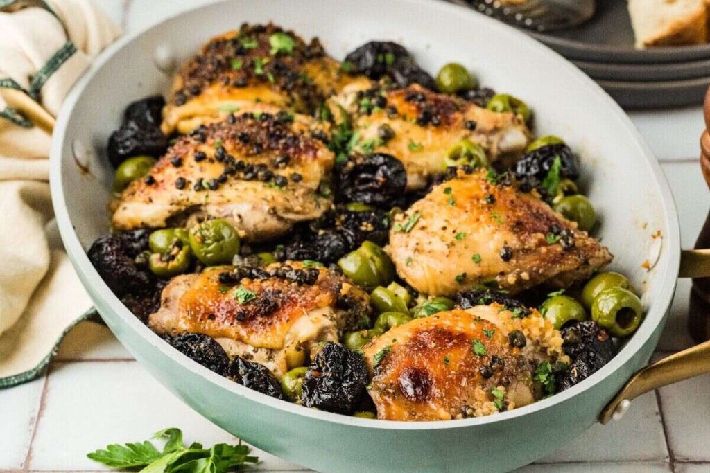 Chicken Marbella skillet with chicken thighs, green olives, prunes, capers, and parsley.