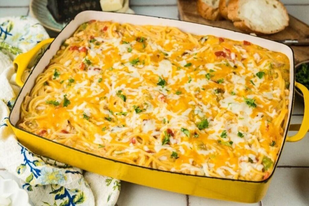 Baked chicken spaghetti casserole with melted cheese and herbs, served with sliced bread.