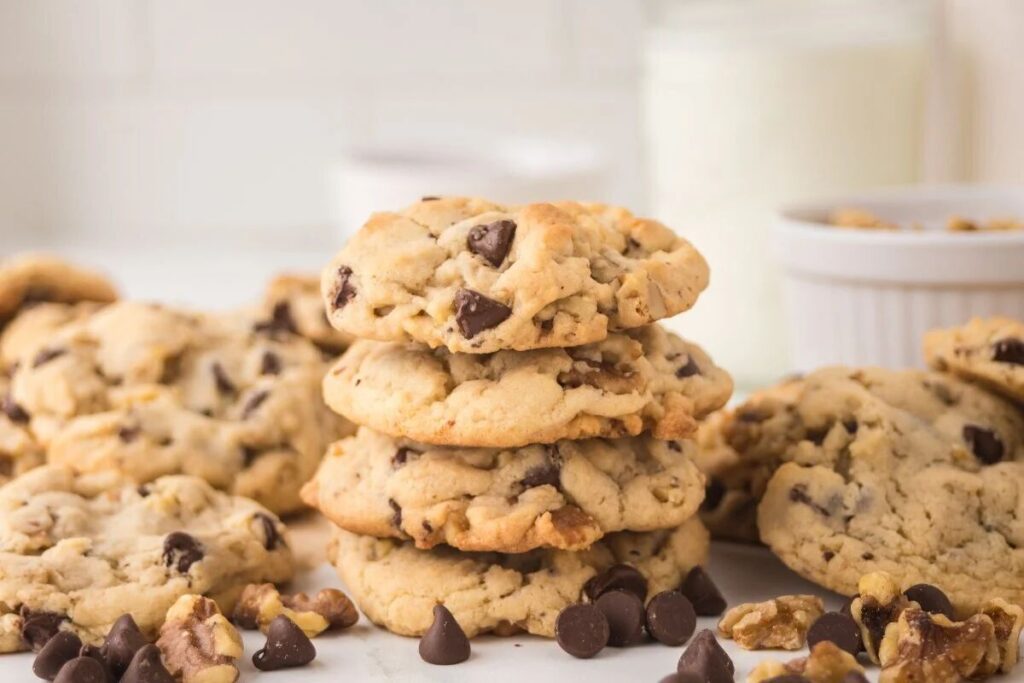 A stack of chocolate chip walnut cookies surrounded by extra cookies, chocolate chips, and walnuts.