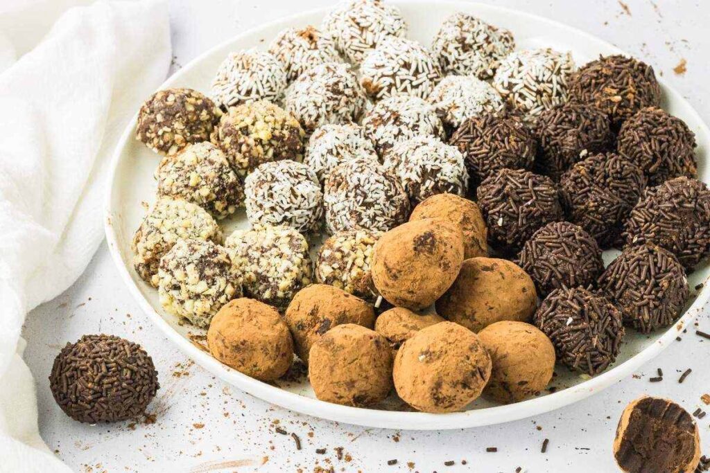 A plate of homemade chocolate truffles with cocoa, coconut, and sprinkles sits on a white surface with a napkin.