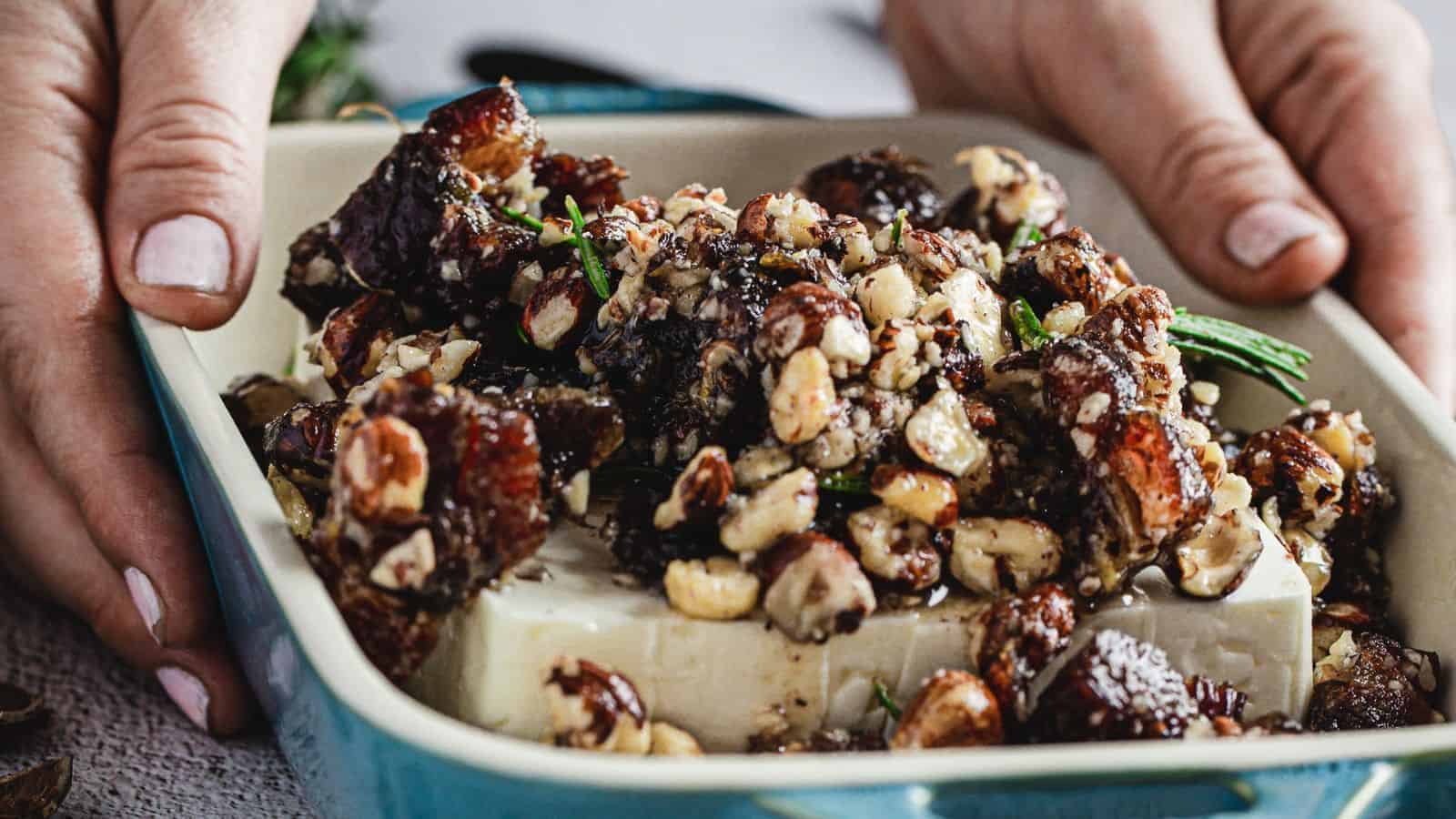 hands holding Creamy Baked Feta Dip Appetizer Recipe With Dates, Hazelnuts, And Honey.