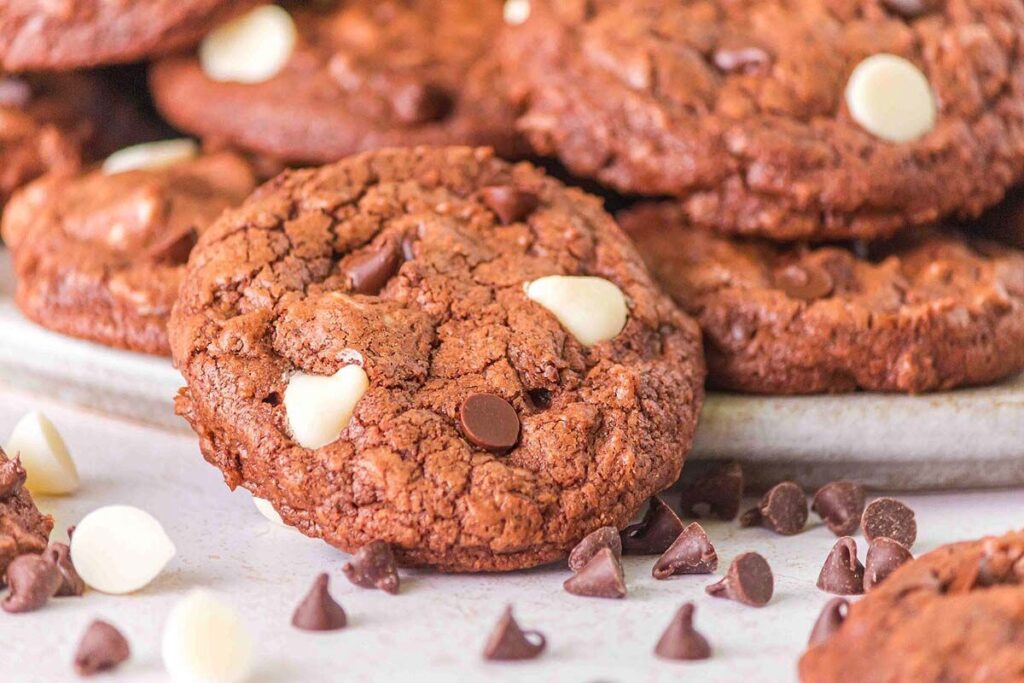 Close-up of devil’s food cookies with white and dark chocolate chips on a plate, with scattered chips around them.