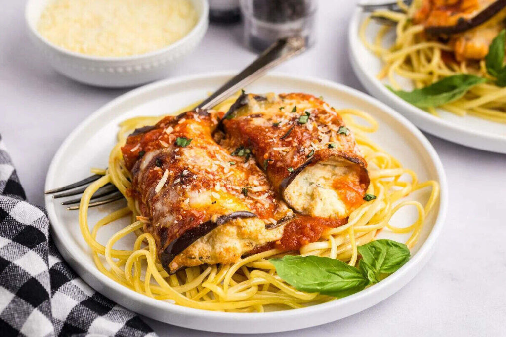 Eggplant rollatini with tomato sauce served over spaghetti and fresh basil.