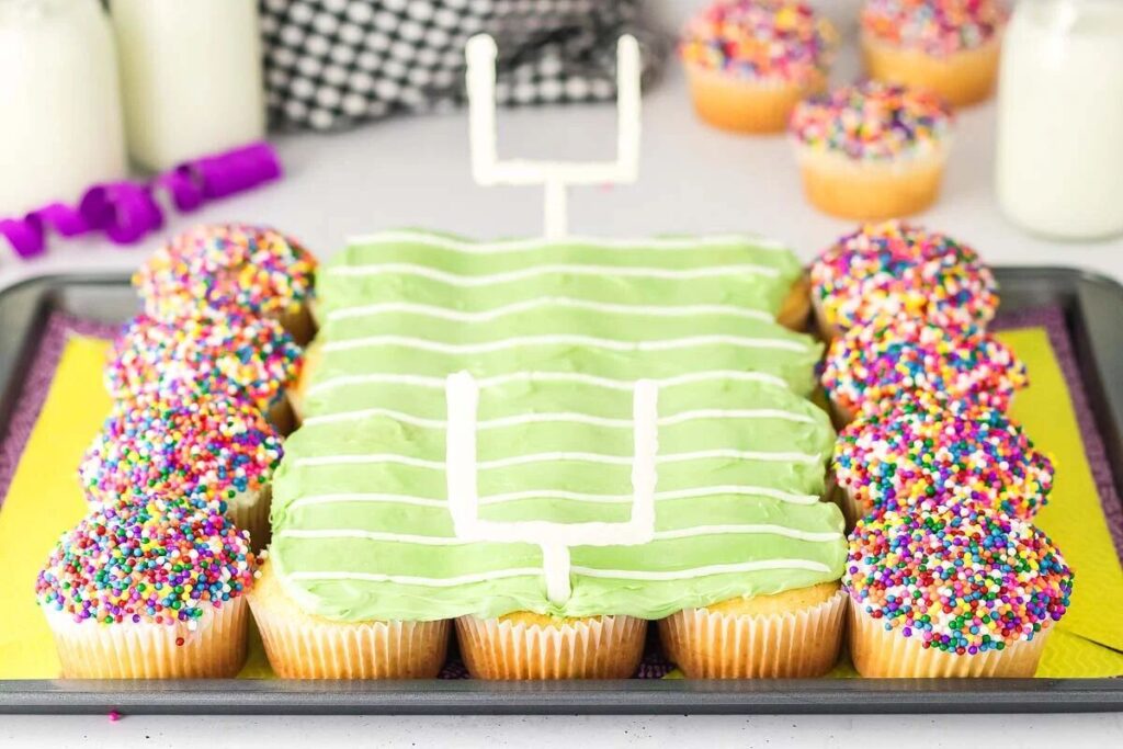 Football stadium cupcakes arranged and decorated like a football field, with green icing in the center and sprinkle-covered cupcakes forming the stands on the sides.