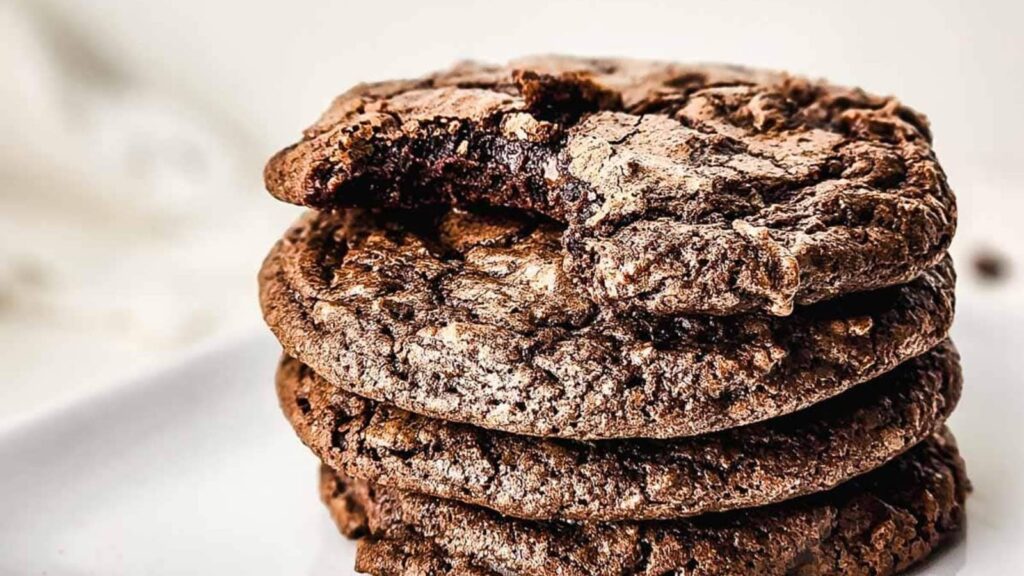 A stack of chocolate cookies, with the top cookie missing a bite, on a white surface.